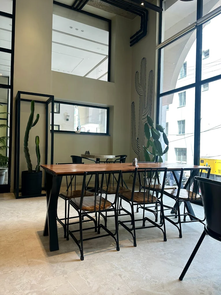 Window-side table at The Urb with cactus mural and tall industrial windows
